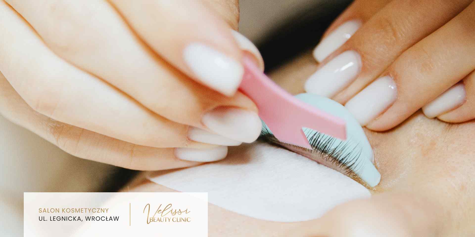Zbliżenie na dłonie kosmetyczki precyzyjnie rozdzielającej rzęsy klientki za pomocą różowego aplikatora podczas zabiegu liftingu.