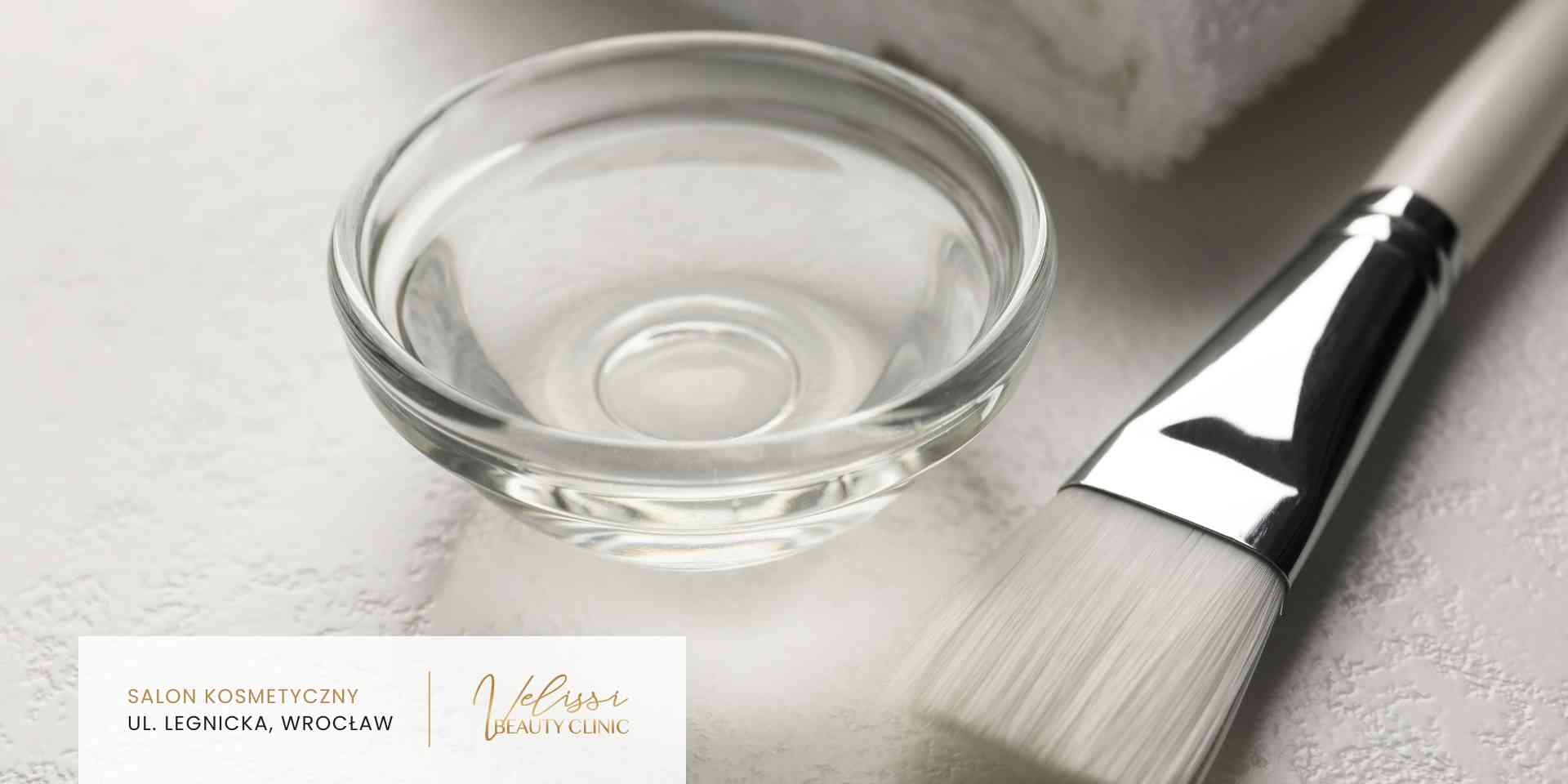 Close-up of a glass bowl and a brushes on a marble surface with a beauty clinic card partially visible nearby.
